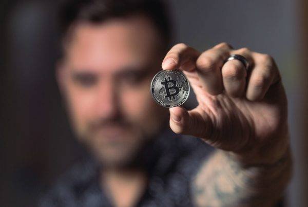 A man holding up a physical coin with the bit coin symbol on it