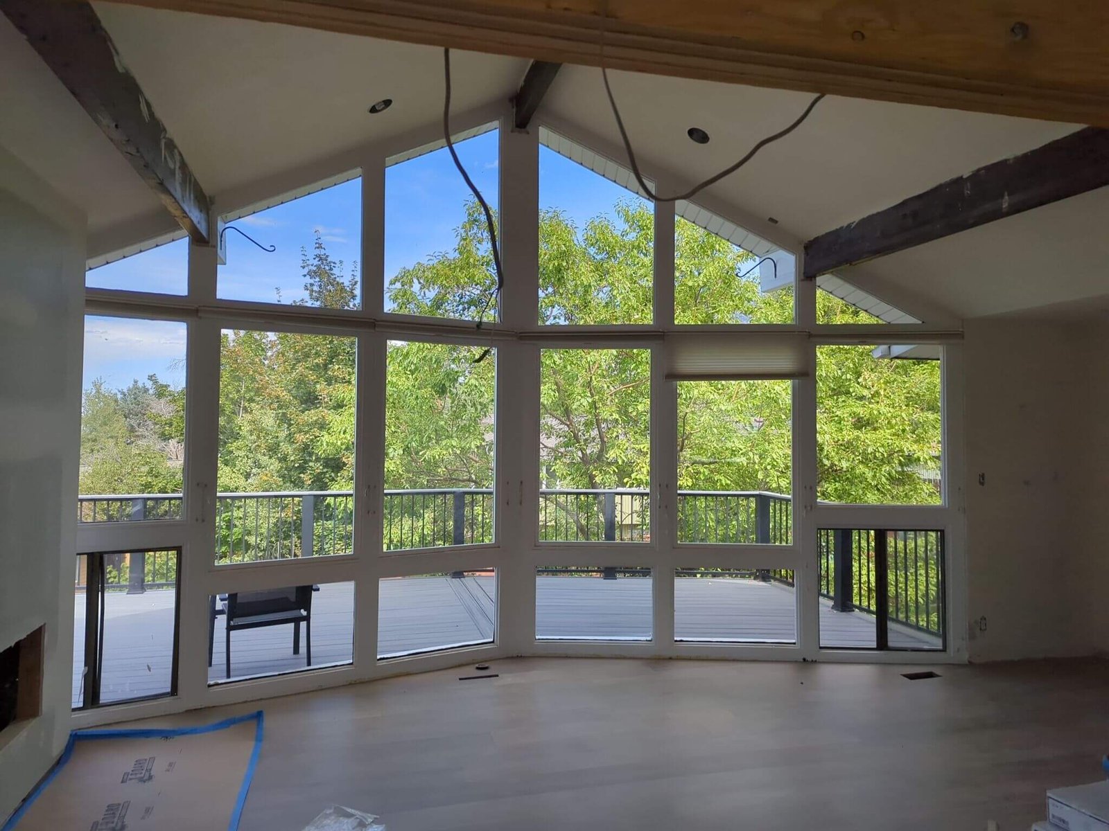Interior view of a home with vaulted ceilings, exposed beams, and floor-to-ceiling windows overlooking a tree-lined deck.