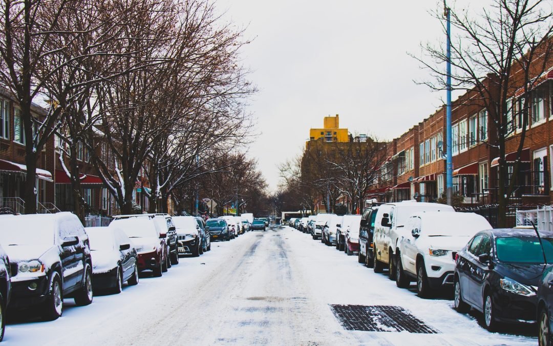 view of a city street with snow on the road and cars parked on both sides of the street covered in snow